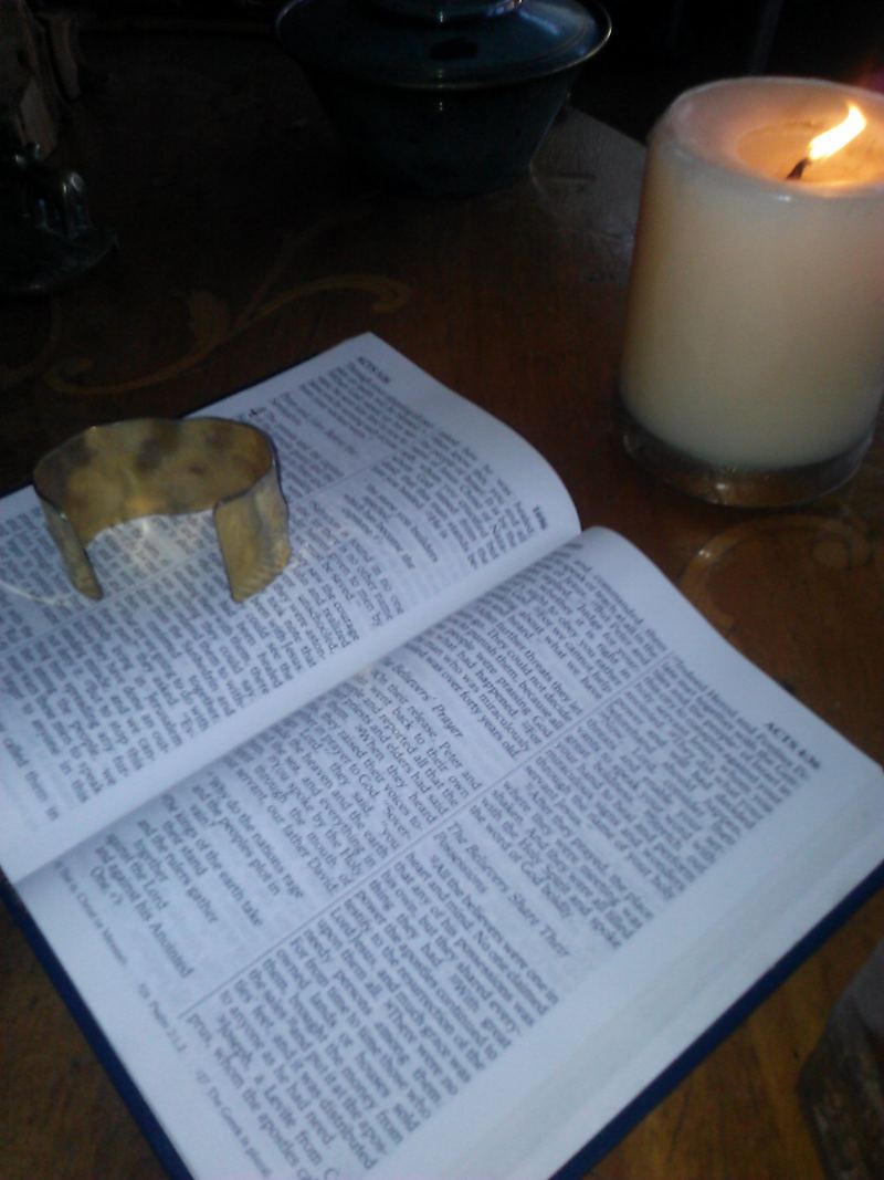 An open Bible on a wooden table beside a lit candle